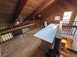 Ein Zimmer mit hohen Decken, Holzboden, einem Schreibtisch, einem Stuhl und einem Fenster.