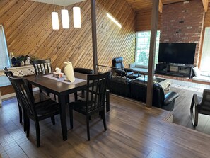 Una habitació amb sostre de fusta, taula de dinar amb cadires, sofà, televisió i llar de foc.