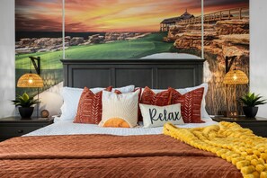 Ein Schlafzimmer mit Blick auf einen Golfplatz, ein Bett mit vielen Kissen, eine gelbe Tagesdecke und zwei Wandlampen.