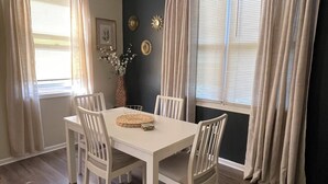 A dining area with a white table and chairs, a vase with flowers, and a dark wall with decorative sunburst mirrors. - Urban 2BR Near LightRail–Easy NYC & MetLife Access (Jersey City)