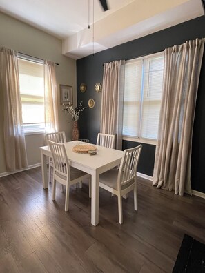 Un coin repas avec une table et des chaises blanches, un vase rempli de fleurs et un mur foncé orné de miroirs décoratifs en forme de soleil.