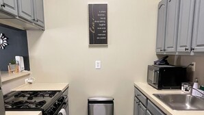 A compact kitchen with grey cabinets, a stainless steel sink, a microwave, a trash bin, and a stove. - Urban 2BR Near LightRail–Easy NYC & MetLife Access (Jersey City)