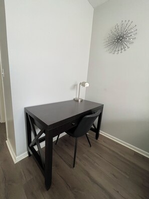 Une pièce d’angle avec un bureau en bois foncé, une chaise noire, un mur blanc et un lampadaire.