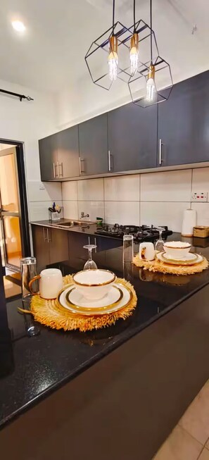 Una cocina moderna con armarios oscuros, encimera negra y una original lámpara colgante hexagonal.