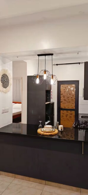 Una cocina moderna con encimera negra, una lámpara colgante hexagonal y una puerta con diseño de placa de circuito.
