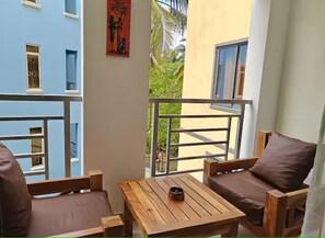 Un balcón con una mesa de madera y dos sillas marrones con cojines, con vista a un edificio de paredes azules y amarillas.