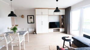 A modern living room with a flat-screen TV, a dining area with a table and chairs, and a large window providing natural light. - Aesthetic Couples Hideaway by the Coast (Dziwnów)