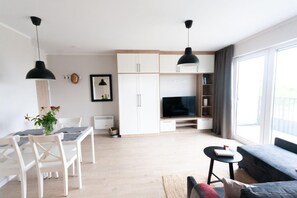 Ein modernes Wohnzimmer mit Flachbildfernseher, einem Essbereich mit Tisch und Stühlen sowie einem großen Fenster, das für natürliches Licht sorgt.
