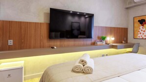 Ein Hotelzimmer mit einem Bett, einem flachbildfernseher an der Wand, einem Nachttisch mit Lampe und einer kleinen Pflanze.