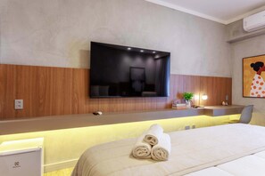 Habitación de hotel con cama, televisor de pantalla plana en la pared, mesita de noche con lámpara y una planta pequeña.