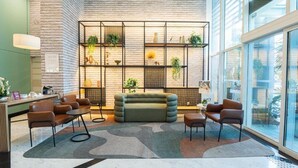 Eine moderne Lobby mit Backsteinwand, einem grünen Sofa, braunen Sesseln und einem Pflanzen-Raumteiler aus Glas.