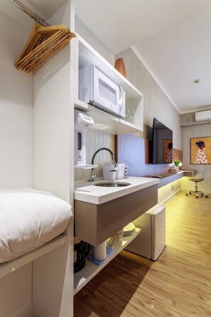 Una kitchenette compacta con microondas, lavamanos y estanterías.