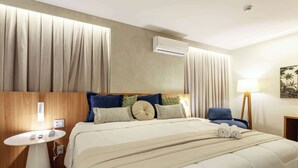 Een hotelkamer met een bed, nachtkastje, lamp en airconditioner.