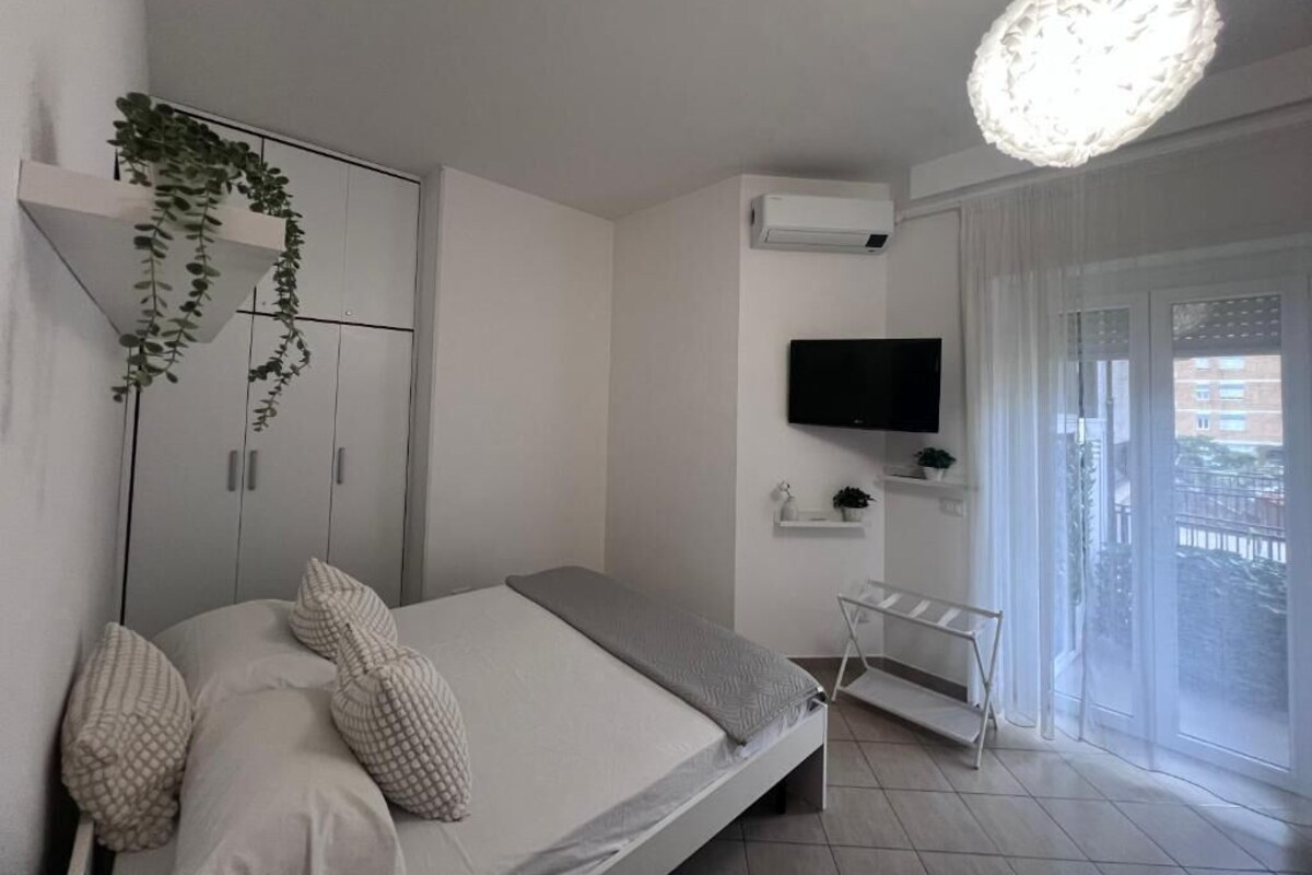 Un dormitorio con cama, televisor, planta y balcón con vistas.