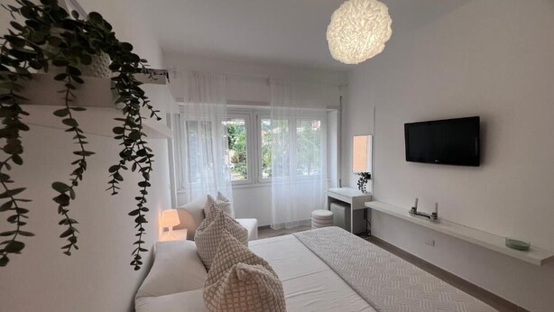 A modern bedroom with a bed, bedside table, TV, and a view of the outdoors. - Terracina Central Rooms (Terracina)