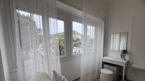 A bedroom with a bed, a desk, a chair, a small stool, and a window with curtains. - Terracina Central Rooms (Terracina)