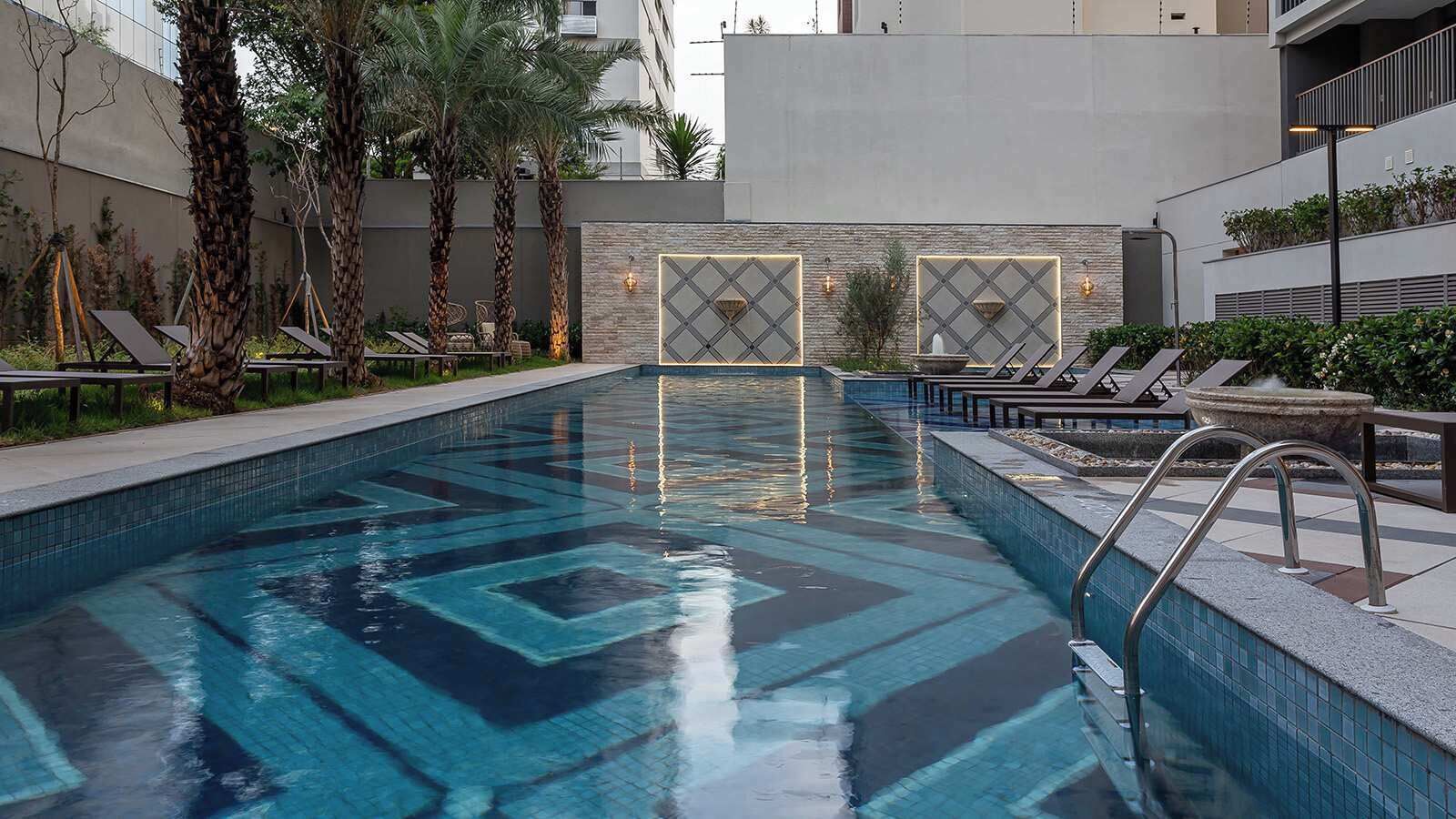 A swimming pool with a geometric tile pattern, surrounded by lounge chairs and palm trees.
