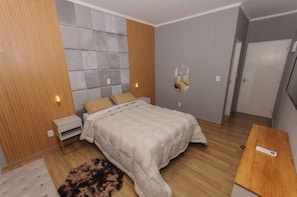 Un dormitorio con cama, mesitas de noche, un espejo, suelo de madera y una puerta.