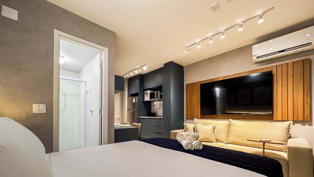 A modern hotel room with a bed, a sofa, a TV, and a kitchenette. - #MY606 | Cyclinn Pinheiros (Pinheiros)
