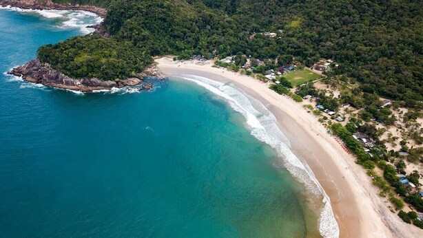 An aerial view of a coastal area with a beach, a small island, and scattered buildings. - @Staycy | Casa com rio privativo em Camburi (Camburí)
