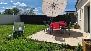 A patio with a table and chairs, an umbrella, and a white chair. - Family home near Chambord (Mont-près-Chambord)