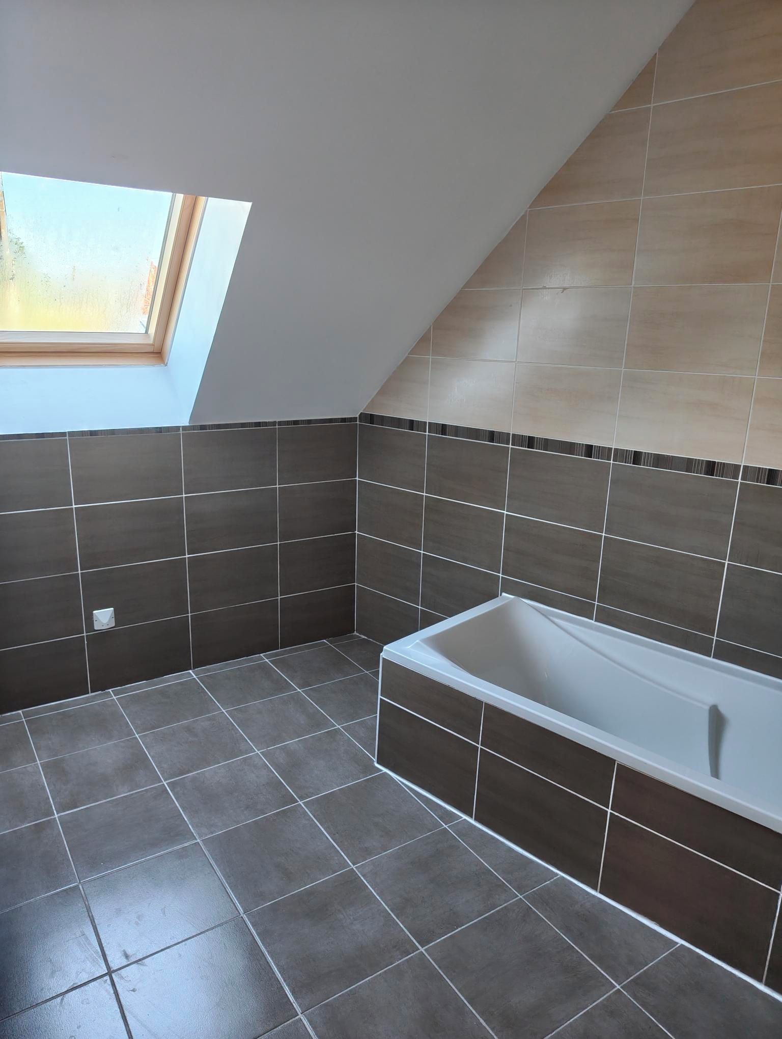 Een moderne badkamer met dakraam, ligbad en donkere betegelde wanden.