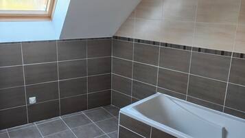 Een moderne badkamer met dakraam, ligbad en donkere betegelde wanden.