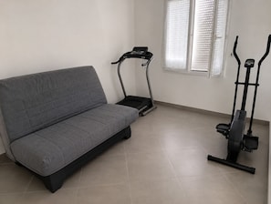 Une piÚce avec un canapé gris, un tapis de course et un vélo elliptique.
