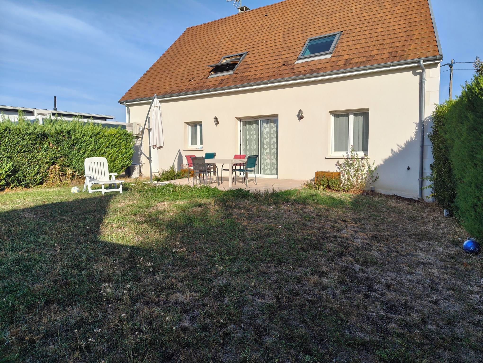 Une maison de plain-pied avec un toit en tuiles, une terrasse dotée de mobilier d’extérieur et une pelouse bien entretenue.