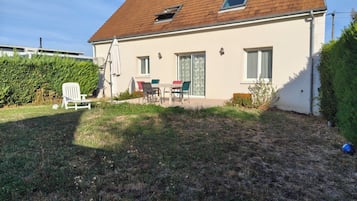 Una casa de un piso con techo de tejas, un patio con mobiliario exterior y un césped bien cuidado.