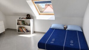 A bedroom with a skylight, a bed with blue bedding, a white bookshelf, and a small dog figurine. - Family home near Chambord (Mont-près-Chambord)