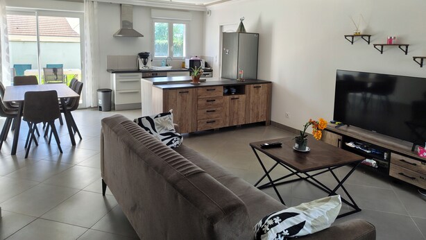 A modern living room with a sofa, coffee table, TV, kitchen area, and dining space. - Family home near Chambord (Mont-près-Chambord)