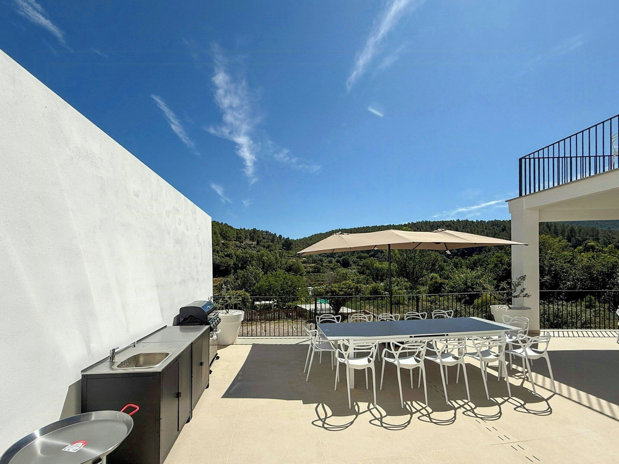 An outdoor patio with a table and chairs, a grill, and a view of a forested hillside.