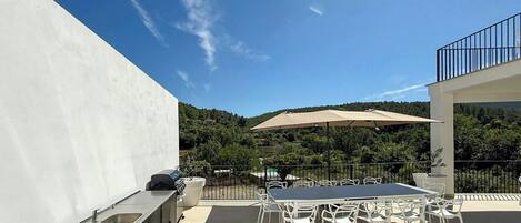 An outdoor patio with a table and chairs, a grill, and a view of a forested hillside.