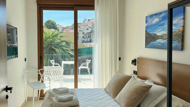 Un dormitorio con cama, un balcón con sillas y vistas a edificios.
