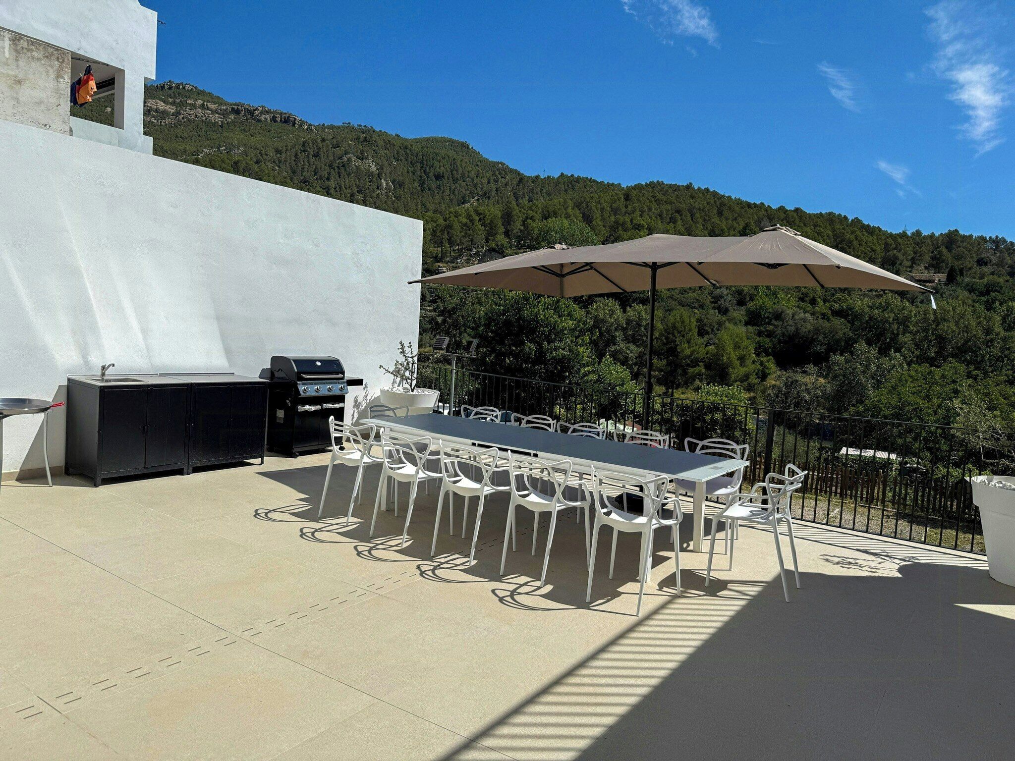 An outdoor patio with a grill, dining table, chairs, and a large umbrella.