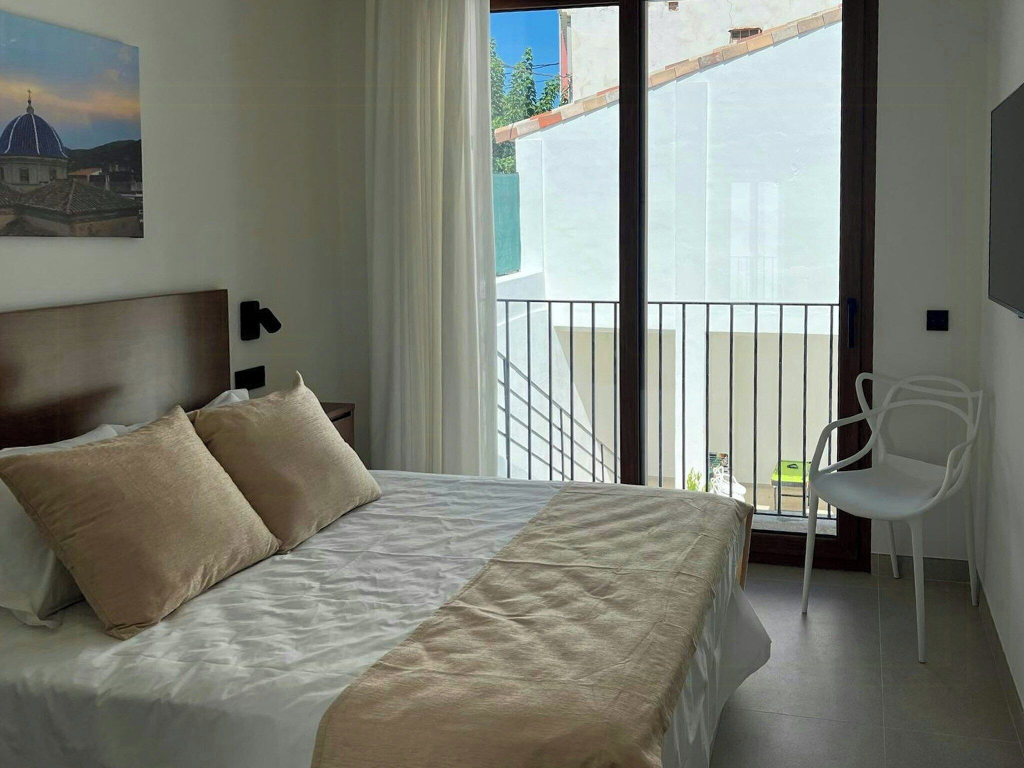 Ein Schlafzimmer mit Bett, Sessel, Nachttisch, einem Bild und einem Balkon mit Geländer.