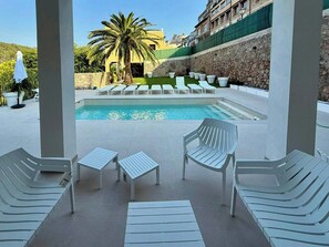 A pool area with white lounge chairs, a palm tree, and a stone wall.