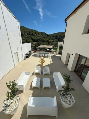 A rooftop terrace with white lounge chairs, a table, and potted plants.