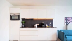 Een moderne keuken met witte kasten, een Bosch oven, een koffiezetapparaat en een blauwe bank in de woonkamer.