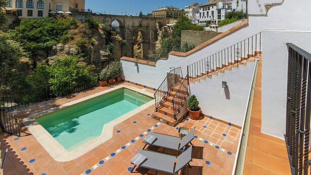 Una piscina en la azotea con una escalera, sillas de descanso y vistas a la ciudad.