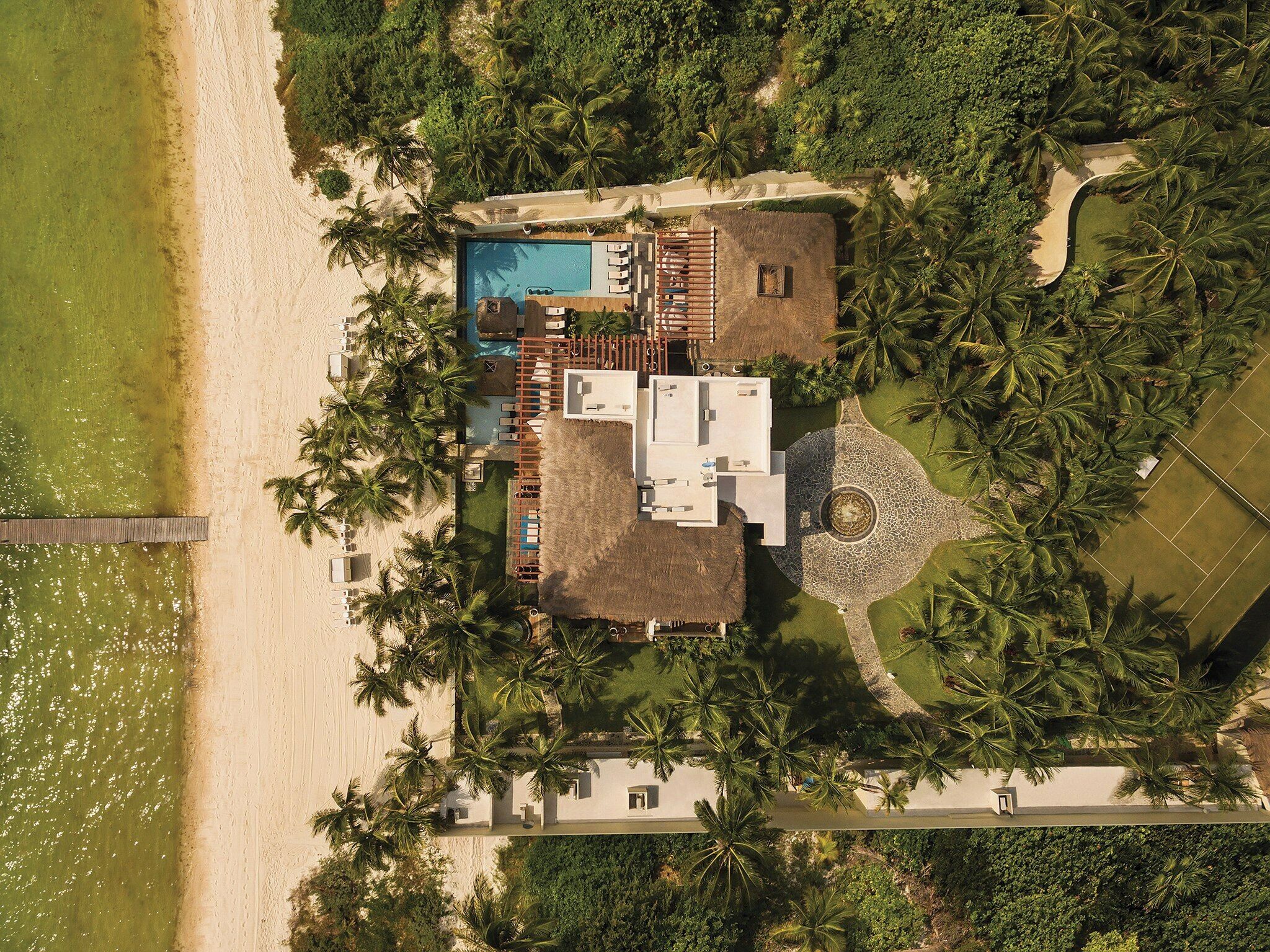 Luftaufnahme eines Resorts mit Pool, Palmen und Strand.