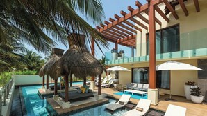 Un área de piscina con sillones de descanso, una estructura de techo de paja y una barandilla de cristal.