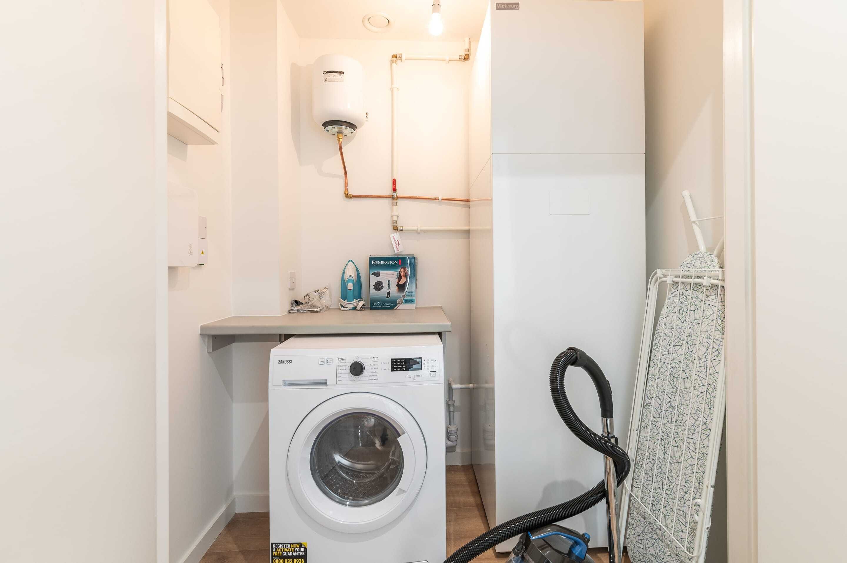 Een kleine wasruimte met een wasmachine, een boiler en een droogrek.