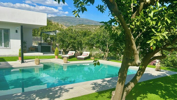 A modern pool with a clear blue pool, surrounded by a well-maintained lawn and a tree.