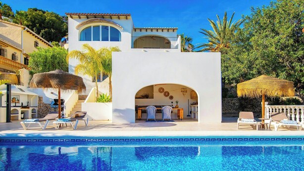 Zona junto a la piscina con sillones de descanso, un área de estar cubierta y un edificio con fachada de piedra.