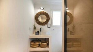 Un baño con un espejo redondo, un lavabo blanco y dos cestas de mimbre sobre un estante blanco.