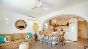 Una sala de estar moderna con un sofá, un espejo redondo y una zona de comedor con taburetes de bar.