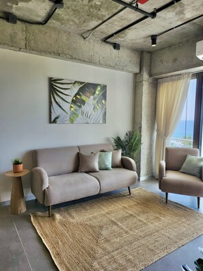 A living room with a sofa, armchairs, a rug, a potted plant, and a painting on the wall. - Zonte Terrace - 2BR Designer Loft with Surf Views (El Zonte)