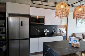 A modern kitchen with stainless steel appliances, a black countertop, and a dining area with a marble table. - Zonte Terrace - 2BR Designer Loft with Surf Views (El Zonte)